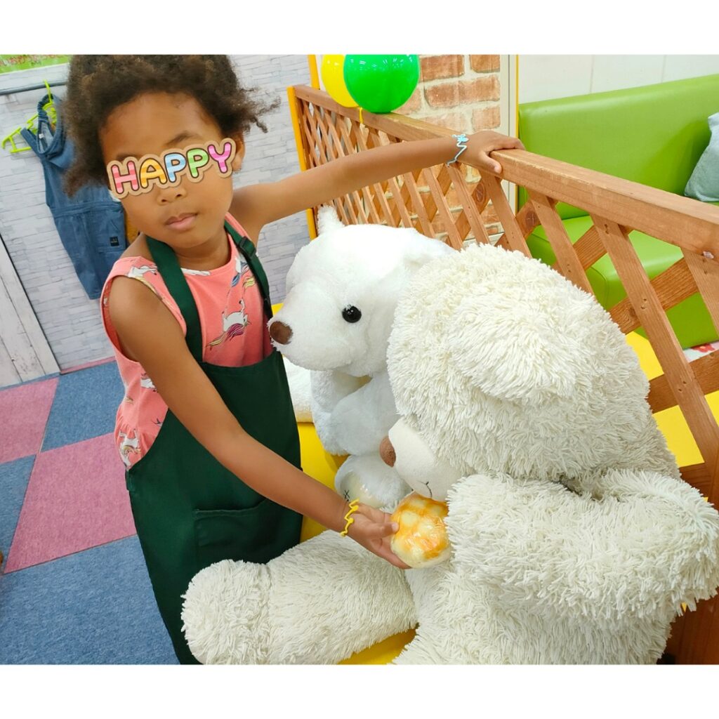 大阪　あそびマーレ　パン屋さんになりきって緑のエプロンを着てシロクマのぬいぐるみに玩具のパンをあげている女の子